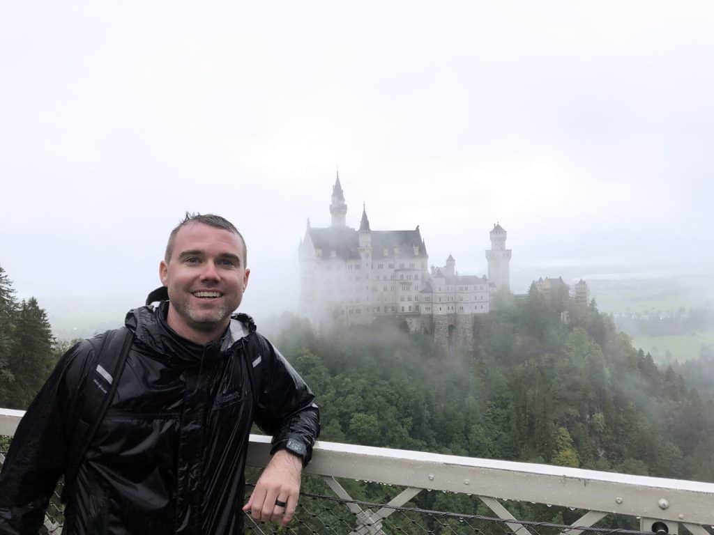 Scenic view of a man smiling at Neuschwanstein Castle in foggy weather, showcasing work at 407&Beyond.