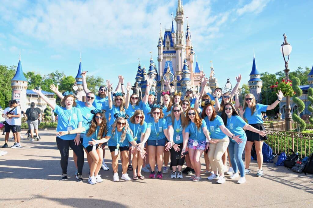 Group of employees celebrating at Disney castle, promoting work at 407&Beyond theme park jobs and team events.