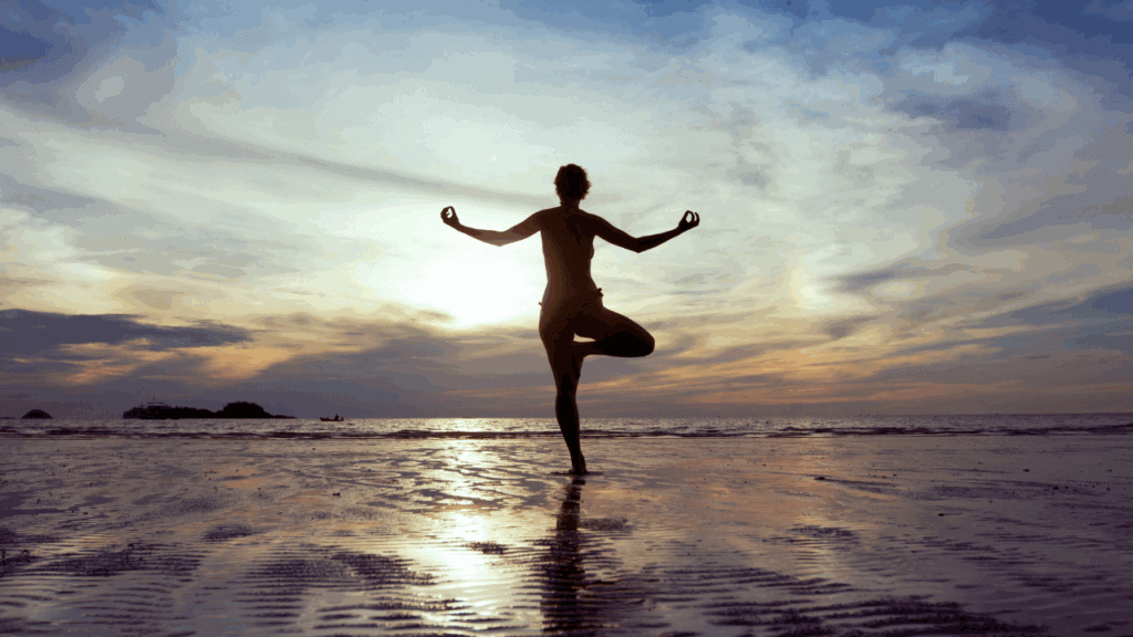 Silhouette of a person practicing yoga on the beach during sunset at 407&Beyond.