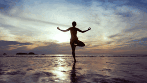 Silhouette of a person practicing yoga on the beach during sunset at 407&Beyond.